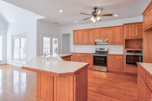 kitchen with tile countertops, stainless steel appliances, a sink, and under cabinet range hood