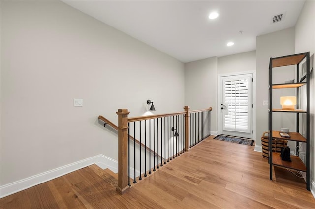 hallway featuring wood finished floors, an upstairs landing, visible vents, and baseboards