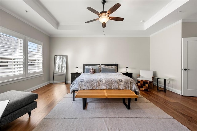 bedroom with a raised ceiling, crown molding, baseboards, and wood-type flooring