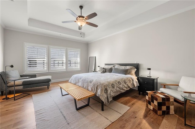 bedroom with baseboards, a tray ceiling, ornamental molding, wood finished floors, and a ceiling fan