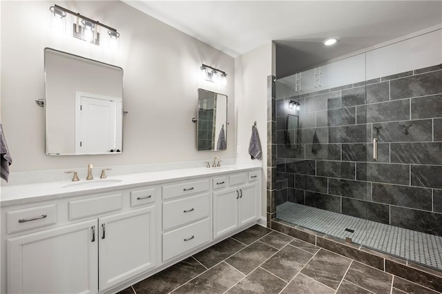 bathroom featuring double vanity, a tile shower, and a sink