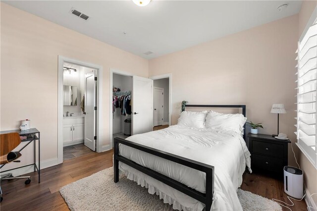 bedroom featuring visible vents, ensuite bathroom, a sink, wood finished floors, and baseboards