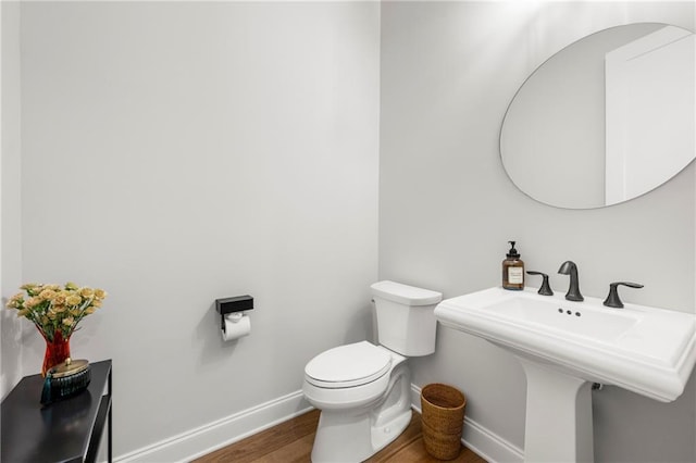 bathroom featuring toilet, wood finished floors, baseboards, and a sink