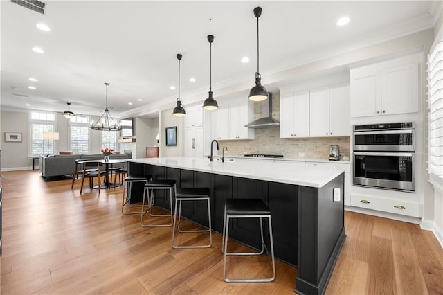 kitchen featuring visible vents, double oven, black stovetop, wall chimney exhaust hood, and a sink