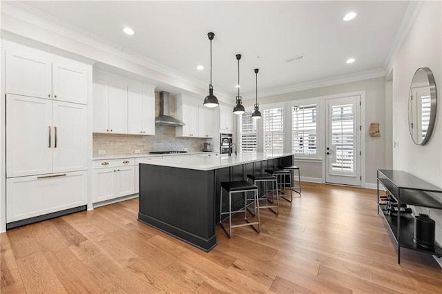 kitchen featuring white cabinetry, wall chimney range hood, light wood finished floors, and ornamental molding