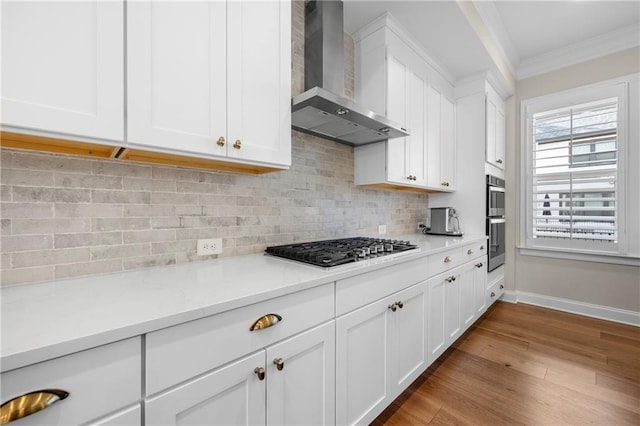 kitchen featuring ornamental molding, backsplash, wood finished floors, appliances with stainless steel finishes, and wall chimney range hood