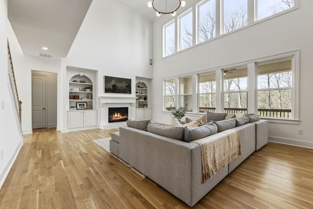 828 Chestnut Pl, Milton, GA 30004 - living room featuring built in shelves, baseboards, a warm lit fireplace, light wood-style floors, and a high ceiling