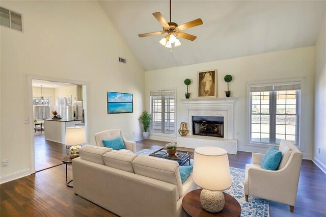 living area featuring visible vents, a fireplace with raised hearth, dark wood-style floors, and a ceiling fan