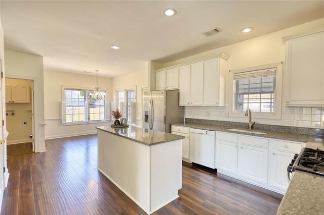 kitchen with visible vents, a kitchen island, white dishwasher, a sink, and stainless steel fridge
