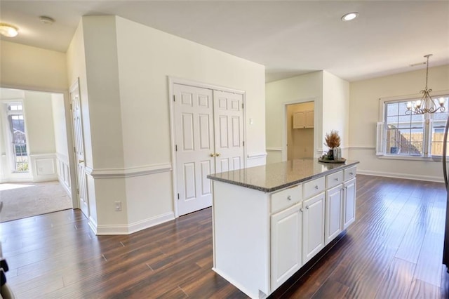 kitchen with dark stone countertops, dark wood-style floors, decorative light fixtures, a notable chandelier, and a center island