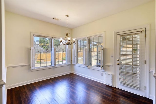 unfurnished dining area featuring an inviting chandelier, dark wood-type flooring, baseboards, and visible vents