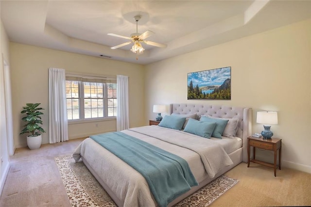 bedroom with visible vents, baseboards, light colored carpet, a raised ceiling, and a ceiling fan