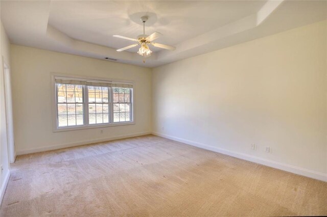 empty room featuring a tray ceiling, light carpet, baseboards, and ceiling fan