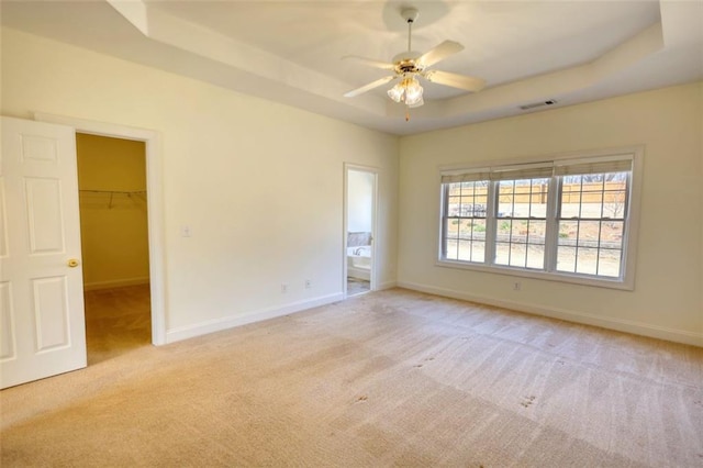 spare room with visible vents, ceiling fan, baseboards, a tray ceiling, and light carpet
