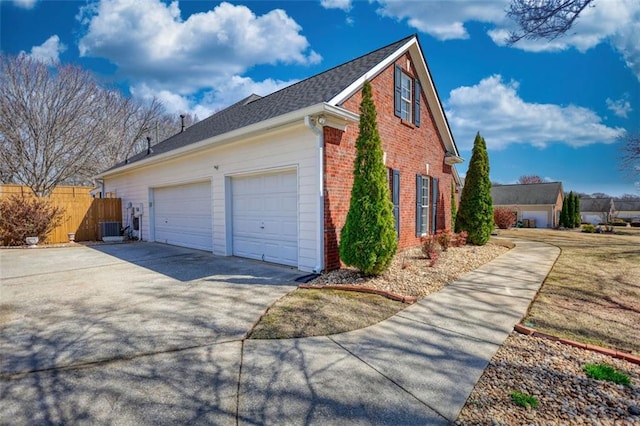 view of side of property with central AC, fence, concrete driveway, an attached garage, and brick siding