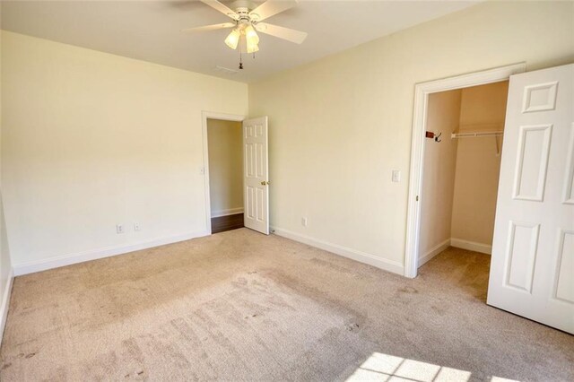 unfurnished bedroom featuring a spacious closet, baseboards, carpet floors, a closet, and a ceiling fan