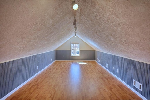 additional living space with visible vents, a textured ceiling, and wood finished floors