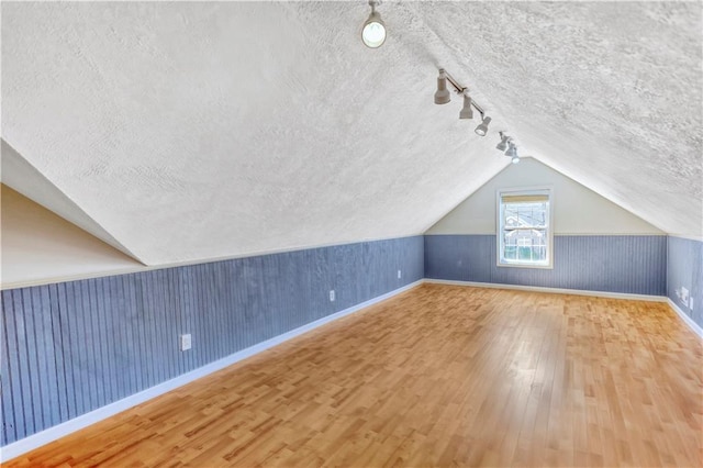 additional living space featuring vaulted ceiling, wood finished floors, baseboards, and a textured ceiling