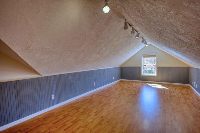 bonus room with vaulted ceiling, wood finished floors, baseboards, and a textured ceiling