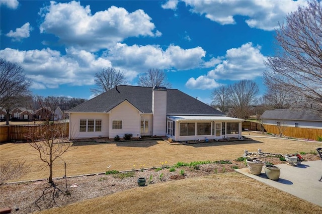 rear view of property featuring a lawn, a sunroom, fence, a shingled roof, and a chimney