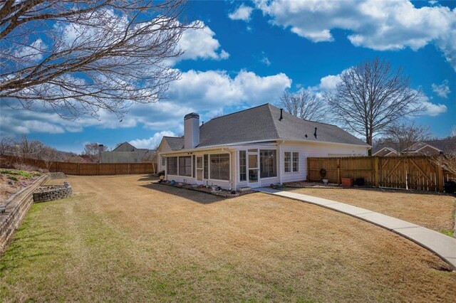 rear view of house with a yard, a fenced backyard, a sunroom, and a chimney