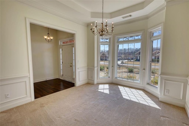 unfurnished dining area with carpet, ornamental molding, a raised ceiling, a decorative wall, and a notable chandelier