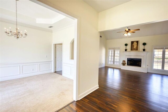 unfurnished living room featuring ceiling fan with notable chandelier, wainscoting, a decorative wall, a brick fireplace, and dark wood-style flooring