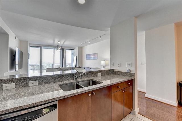 kitchen featuring light stone counters, sink, stainless steel dishwasher, and light hardwood / wood-style flooring