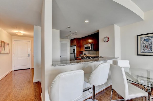 kitchen featuring kitchen peninsula, appliances with stainless steel finishes, light stone countertops, a kitchen breakfast bar, and light hardwood / wood-style floors