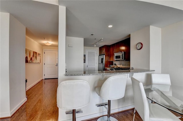 kitchen with a kitchen breakfast bar, stone countertops, light hardwood / wood-style floors, kitchen peninsula, and stainless steel appliances