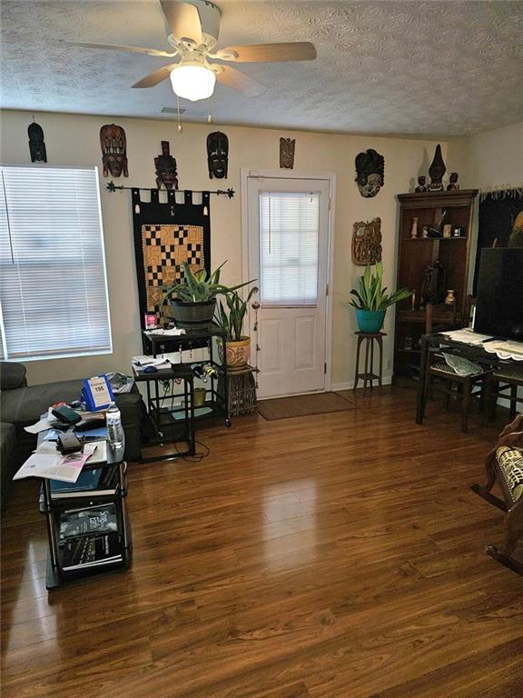 living area with a textured ceiling, wood finished floors, and a ceiling fan