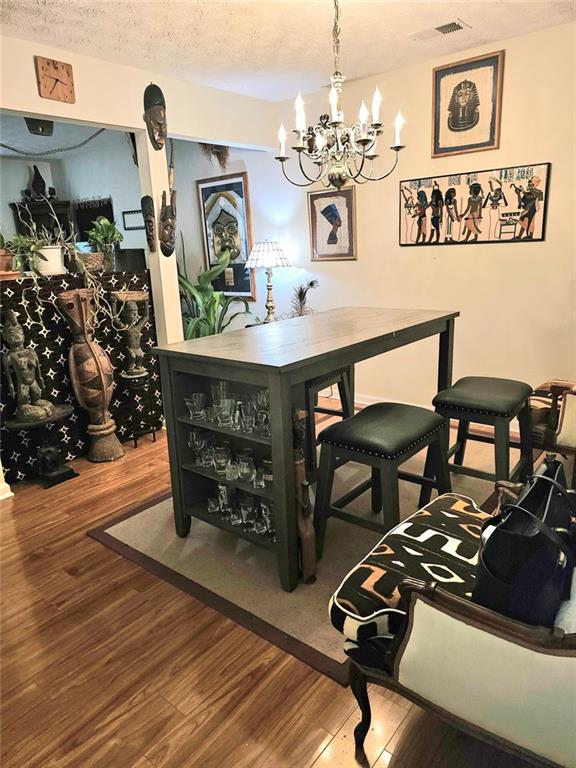 dining space featuring visible vents, a textured ceiling, wood finished floors, and a chandelier