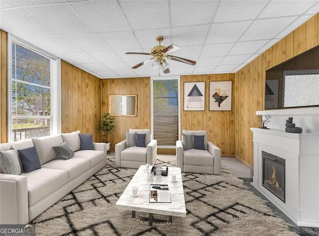 living area featuring a glass covered fireplace, wood walls, and a ceiling fan