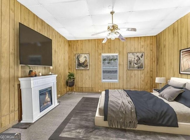 carpeted bedroom with a glass covered fireplace and wooden walls