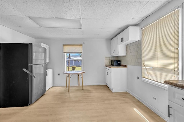 kitchen featuring tasteful backsplash, white cabinetry, freestanding refrigerator, light wood-style floors, and stacked washer / drying machine