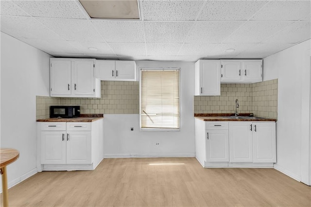 kitchen featuring dark countertops, light wood finished floors, baseboards, black microwave, and white cabinets