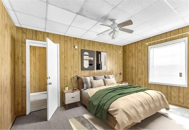 carpeted bedroom featuring wooden walls and a ceiling fan