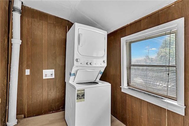 laundry area featuring laundry area, stacked washer / dryer, light wood-style flooring, and wood walls