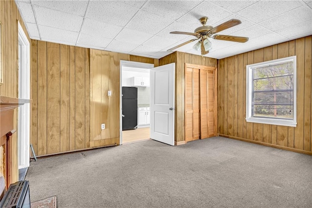 unfurnished room with carpet flooring, a ceiling fan, baseboards, and wood walls