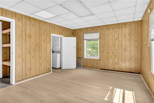 interior space with wood finished floors, baseboards, a drop ceiling, stacked washer / drying machine, and wood walls