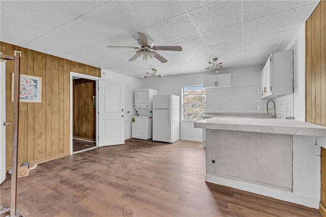 kitchen with wood finished floors, a peninsula, freestanding refrigerator, ceiling fan, and stacked washer and clothes dryer