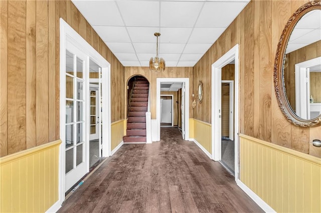 hall with a drop ceiling, wood finished floors, wood walls, wainscoting, and stairs