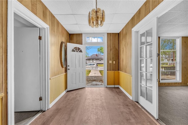 foyer featuring a drop ceiling, wood finished floors, a notable chandelier, and wood walls