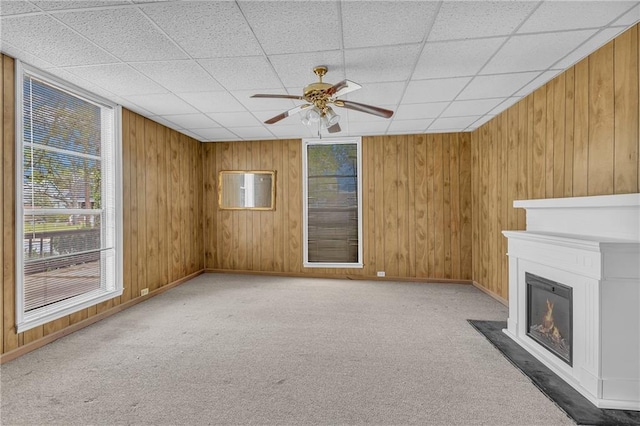 unfurnished living room with a glass covered fireplace, carpet, wood walls, and ceiling fan