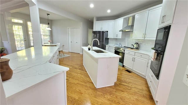 kitchen with black appliances, an island with sink, pendant lighting, wall chimney range hood, and white cabinets