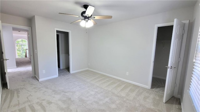 unfurnished bedroom featuring a spacious closet, light colored carpet, a closet, and ceiling fan