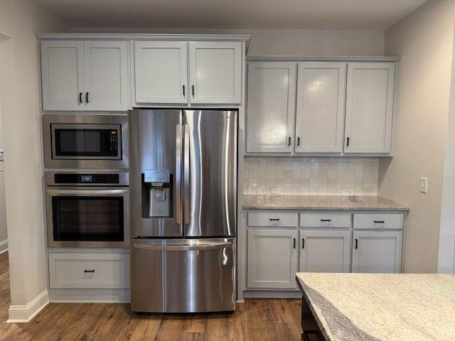 224 Crest Creek Way, Villa Rica, GA 30180 - kitchen featuring appliances with stainless steel finishes, decorative backsplash, dark wood-type flooring, and light stone counters