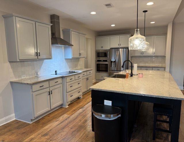 224 Crest Creek Way, Villa Rica, GA 30180 - kitchen with appliances with stainless steel finishes, wall chimney exhaust hood, wood finished floors, light stone counters, and recessed lighting