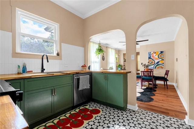 kitchen featuring green cabinetry, stainless steel dishwasher, a sink, arched walkways, and wood counters