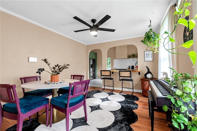 dining area with arched walkways, wood finished floors, ceiling fan, ornamental molding, and healthy amount of natural light